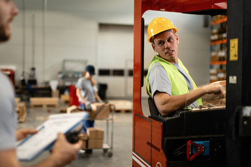 Forklift operator talking with a foreman in industrial warehouse.