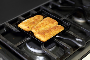 Fish sticks baked on a raclette pan resting on the stove top.