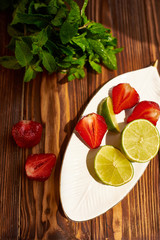 lime strawberry mint ingredients for making lemonade on white plate on wooden table