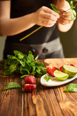 cooking of cooling summer cocktail with strawberries, ice and mint and around the berries are ripe fresh strawberries and lime