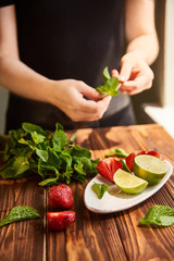 cooking of cooling summer cocktail with strawberries, ice and mint and around the berries are ripe fresh strawberries and lime