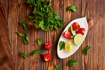 lime strawberry mint ingredients for making lemonade on white plate on wooden table