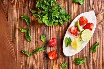 cooking of cooling summer cocktail with strawberries, ice and mint and around the berries are ripe fresh strawberries and lime