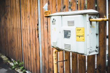 Silver gas meter with yellow pipes hanged outside on a house fence – Utility counter that...