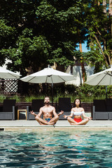 attractive woman and handsome man meditating near swimming pool