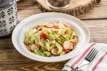 Plate of healthy green garden salad with fresh vegetables on white plate on wooden table