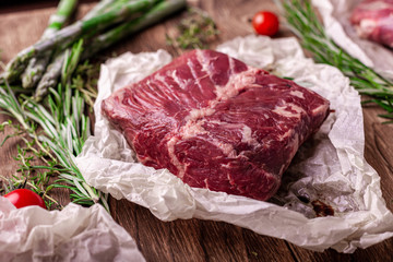 Raw hanging tender beef BBQ steak on wooden Board with rosemary and asparagus and tomatoes. wooden background, top view