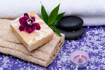 Obraz na płótnie Canvas Spa Wellness Concept. Natural Loofah Sponge, Almond Goat milk Soap, Basalt Stones, Bamboo, Orchid and Lavender Tea Light Candle on purple background.