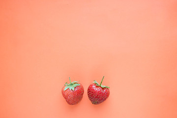 Two strawberries on an orange background, top view