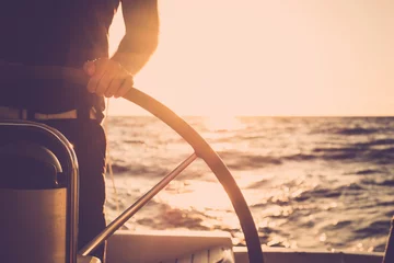 Gordijnen Close up of man's hand on sail boat helm - marine ship lifestyle concept of travel for beautiful holiday destination - alternative people life - sunset and sunlight in background on the ocean © simona