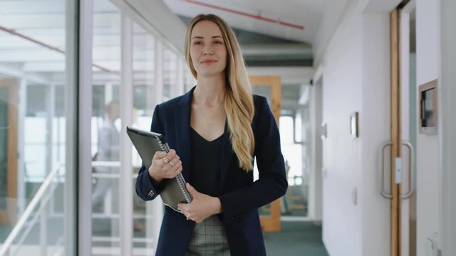 attractive blonde business woman smiling walking through office holding tablet computer enjoying successful leadership career in corporate workplace 4k  
