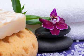 Fototapeta na wymiar Spa Wellness Concept. Natural Foam Bath&Shower Sea Sponge, Almond Goat's milk Soap, Basalt Stones, Bamboo and Orchid Flower on purple background.