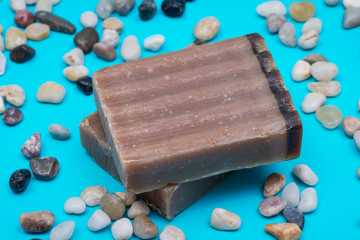 Handmade ultra-moisturizing Frankincense and Myrrh  Scented Goat's Milk Bar Soap decorated with small stone Pebbles on bright blue background.
