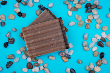Handmade ultra-moisturizing Frankincense and Myrrh  Scented Goat's Milk Bar Soap decorated with small stone Pebbles on bright blue background.