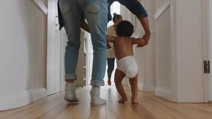 baby taking first steps learning to walk with mother and father teaching toddler at home enjoying parenthood - Powered by Adobe