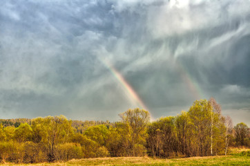 Colorful double Rainbow on cloudy sky over forest after spring rain