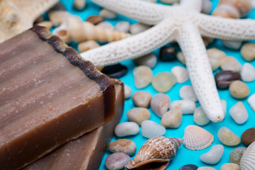 Handmade moisturizing Frankincense & Myrrh Goat's Milk Bar Soap decorated with small Pebbles, Sea Stars and Sea Shells on bright blue background.
