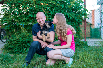Naklejka na ściany i meble Young happy couple with a funny puppy of a German shepherd. A girl and a guy on a green lawn near the house with a new dog. Buying a pet. The joy of first meeting. Copy spase