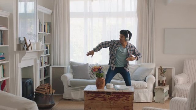 Happy Young Man Dancing At Home Celebrating Success Listening To Music Wearing Headphones Having Fun Dance In Living Room On Weekend 