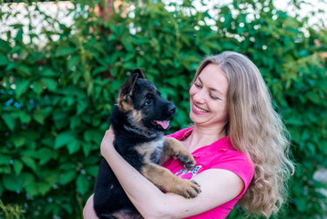 Naklejka na ściany i meble Portrait. Happy girl holding a small puppy German shepherd and smiles. Purchase and purchase of a dog, the joy of the first meeting with the animal. On a green blurred background with copy space