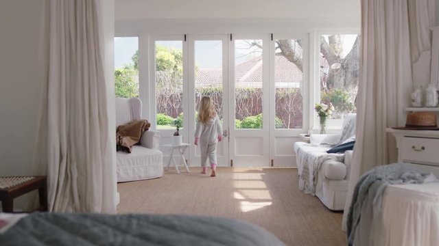 cute little girl in bedroom looking out window enjoying beautiful weekend morning at home wearing pajamas