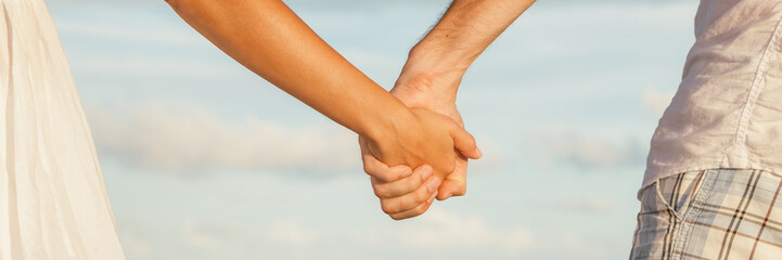 Banner background of couple holding hands dating romantic sunset beach walk panoramic.