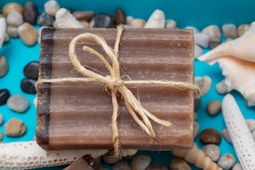 Handmade moisturizing Frankincense & Myrrh Goat's Milk Bar Soap decorated with small Pebbles, Sea Stars and Sea Shells on bright blue background.