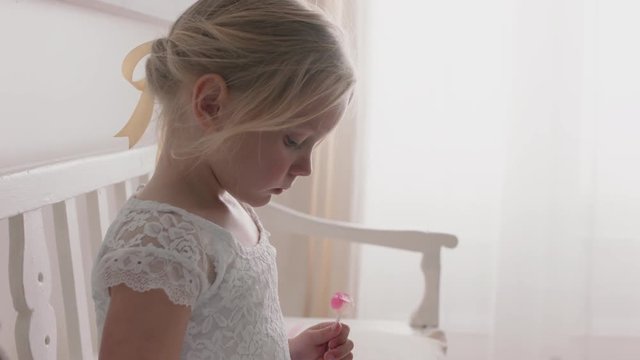beautiful little girl using smartphone watching online entertainment sitting on bench with teddy bear eating lollipop at home 4k footage