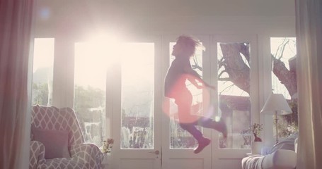 happy little boy jumping off sofa having fun playing game of pretend child in playful mood enjoying weekend morning at home with sunlight shining through window childhood imagination 4k footage - Powered by Adobe