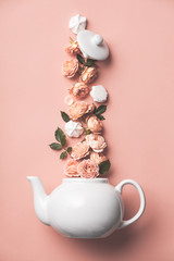 Creative layout made of whte tea pot with orange roses and merengues on pink background