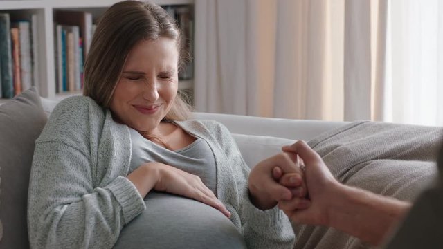 young pregnant woman going into labor having contractions nervous husband helping wife breath calmly through pregnancy pain relaxing on sofa at home