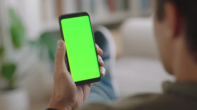 young man using smartphone watching green screen enjoying entertainment on mobile phone chroma key display vertical orientation 4k footage