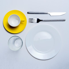 coffee cup fork fork knife and glass on a white table.