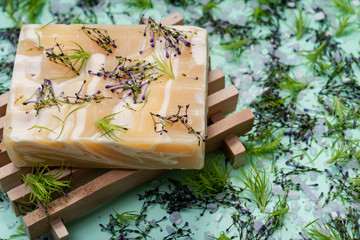 Wooden Soap Holder with Handmade ultra-moisturizing Almond Scented Goats Milk Bar Soap decorated with flower sprinkles confetti on green background.