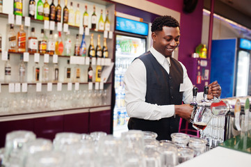 African american bartender at bar pouring from tap fresh beer into the glass in pub.