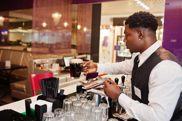African american bartender at bar hold fresh dark beer at glass in pub.