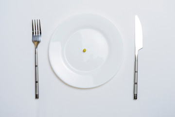diet concept. pea on an empty white plate with knife and fork