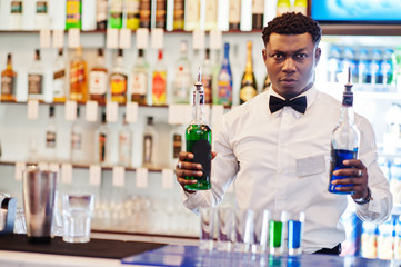 African american bartender at bar making coctails on shots. Alcoholic beverage preparation.