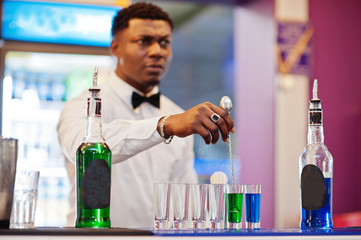 African american bartender at bar making coctails on shots. Alcoholic beverage preparation.