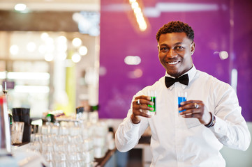 African american bartender at bar holding two coctail shots. Alcoholic beverage preparation.