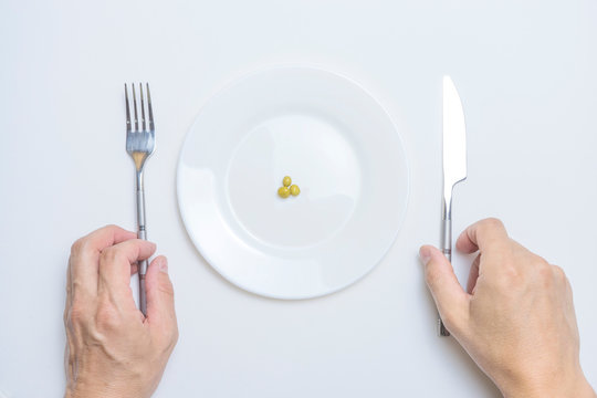 Healthy food theme: hands holding knife and fork on a plate with green peas on a white table top view