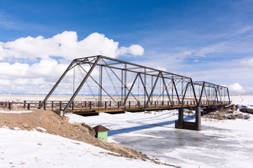 Obraz premium Costilla County, Colorado - February 21, 2019: An 1892 wrought iron bridge spanning the Rio Grande in winter with snow, ice, blue sky, clouds. Built by the Wrought Iron Bridge Co. of Canton, Ohio.