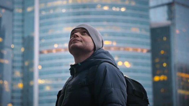 a young man with a backpack and a hat looks up on the background of fire from skyscrapers
