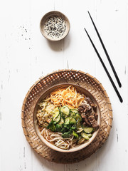 Cold Korean kuksi soup with vegetables, scrambled eggs, beef and noodles in a bowl and chopsticks on a white wood background. Top view