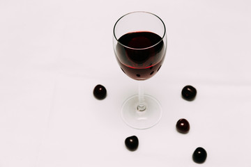 A glass of cherry wine on a red and white background and cherry berries.