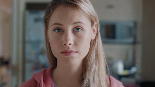 portrait beautiful blonde teenage girl in kitchen at home looking serious expression