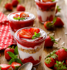 Strawberry layered dessert, healthy dessert with fresh strawberries, natural yoghurt, strawberry mousse and granola in glass dishes on a wooden table. Delicious and nutritious dessert or breakfast