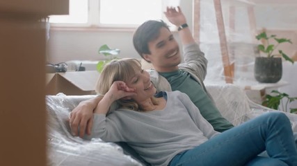 young couple moving into new house together carrying furniture relaxing on sofa resting after successful move enjoying teamwork 4k footage - Powered by Adobe