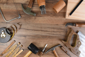 High angle closeup of a large group of tools arranged on a wood workbench around a blank space in...