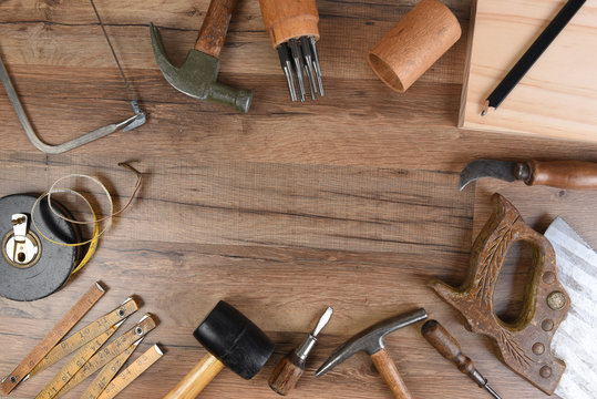 High angle closeup of a large group of tools arranged on a wood workbench around a blank space in the middle